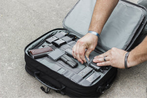 Person organizing items in a black suitcase on a concrete surface
