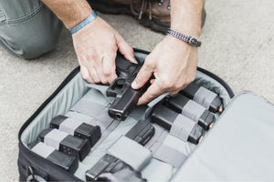 Person handling a handgun and ammunition in an open suitcase.