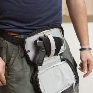 Person wearing a tactical vest with a gun holster on a neutral background