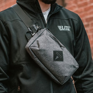 Person wearing a black jacket with 'Elite Survival Systems' branding, holding a gray crossbody bag.
