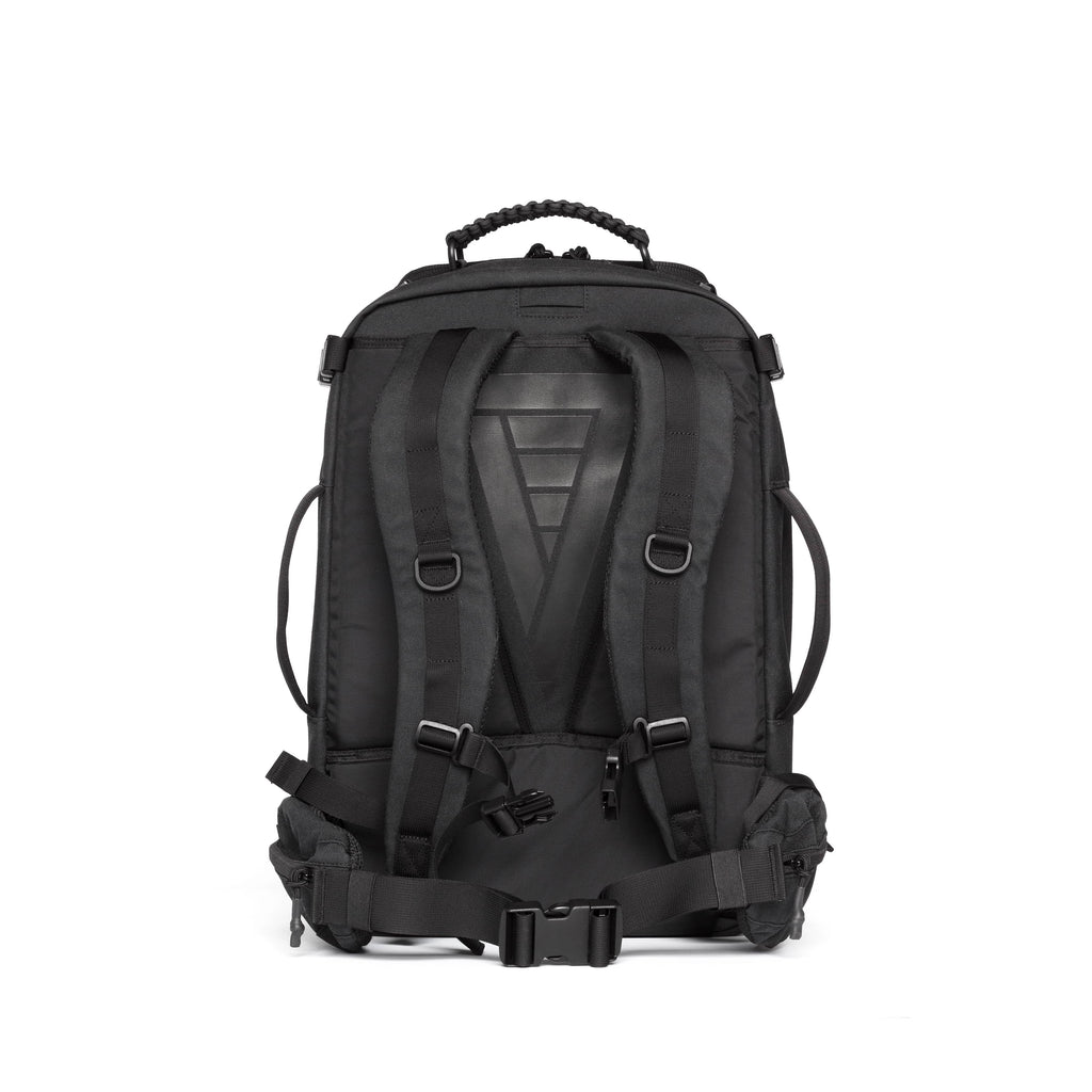 A black tactical backpack shown from the back, featuring padded shoulder straps, a textured back panel, compression straps, and a top carry handle, set against a plain white background.