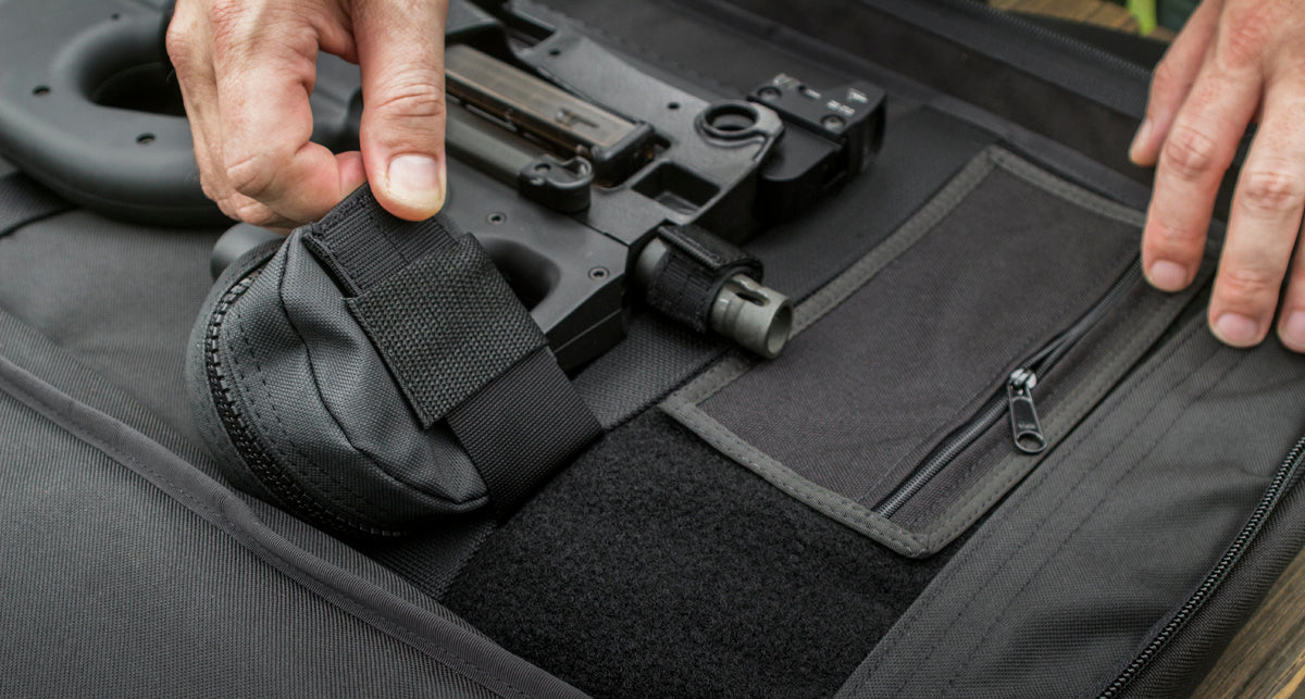 Close-up of a black tactical pouch with a hook-and-loop strap being attached to a firearm magazine, placed inside a black tactical bag with a zippered pocket.
