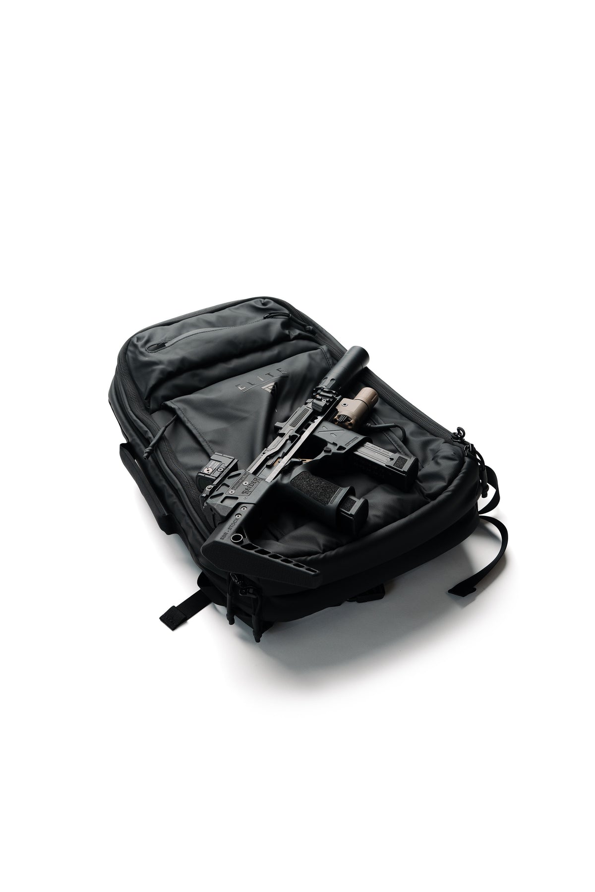A black tactical backpack shown open on a white background, containing a black rifle with a scope and accessories.