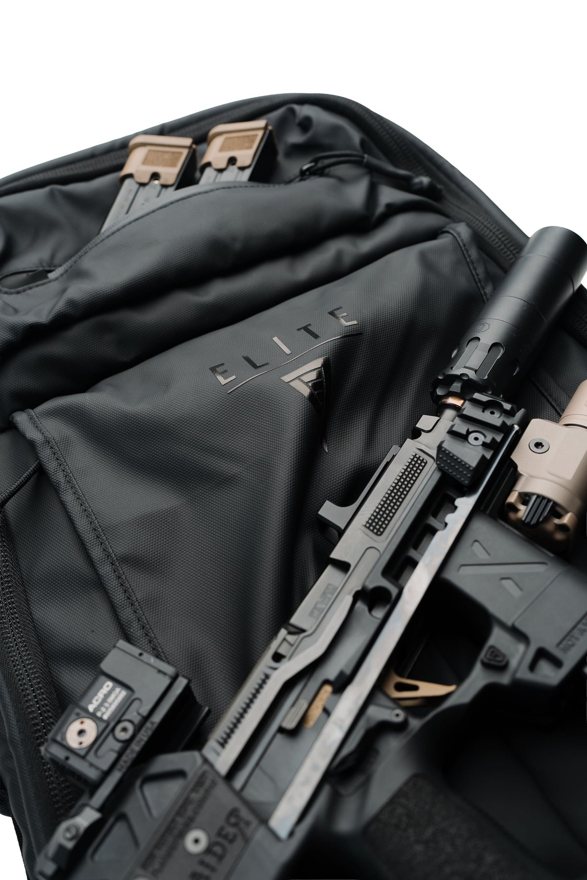 A close-up of a black tactical backpack with a handgun and a rifle laid across it, showing the ELITE logo on the front pocket against a white background.