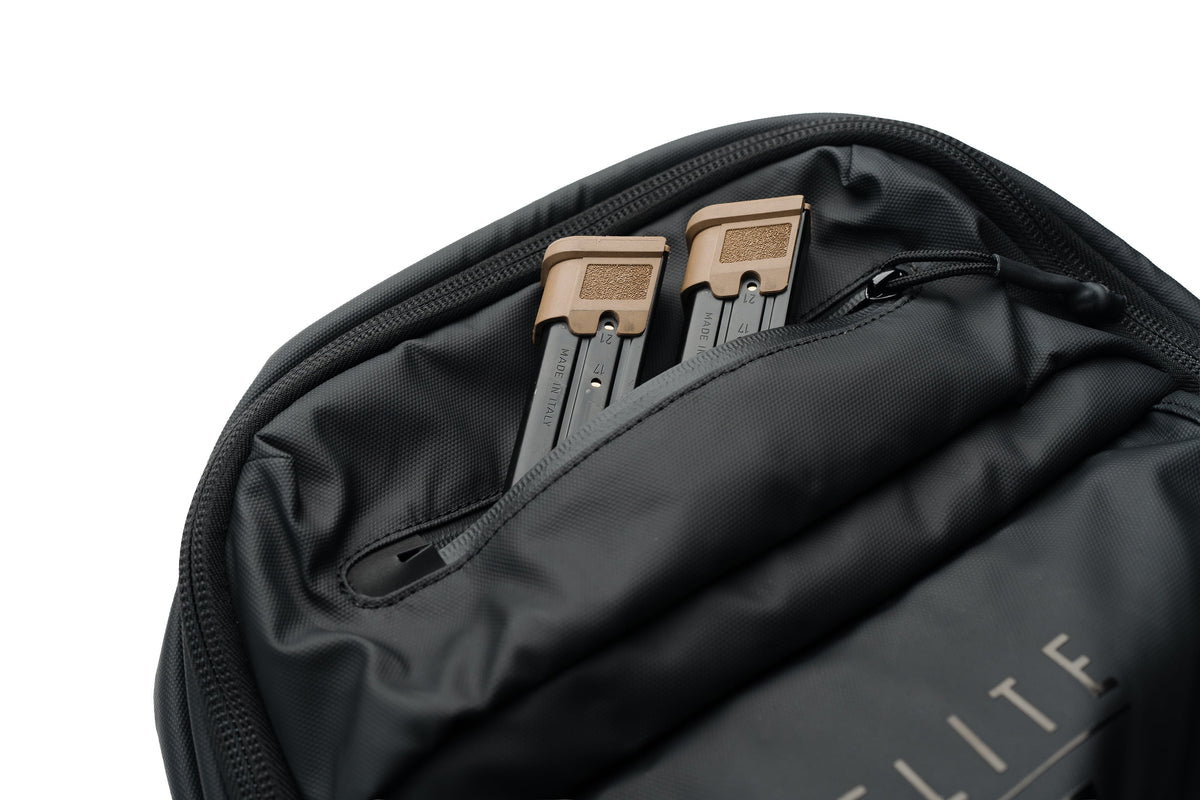 Close-up of a black backpack interior showing a zippered pocket with two tan-and-black credit cards and partial white 'ELITE' branding on the fabric.