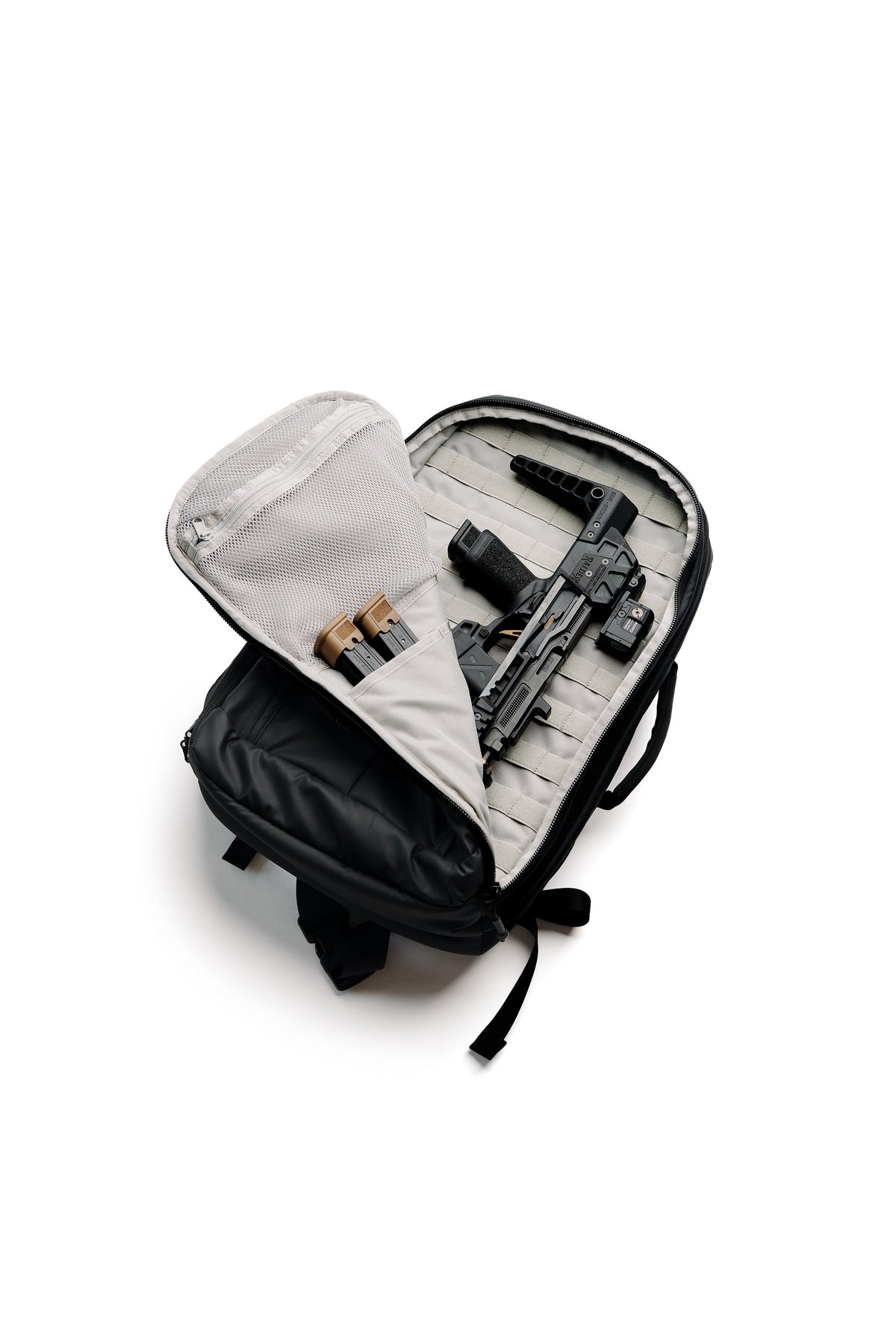 An open black and gray tactical backpack shown from above, revealing a firearm and ammunition stored inside molded compartments, on a white background.