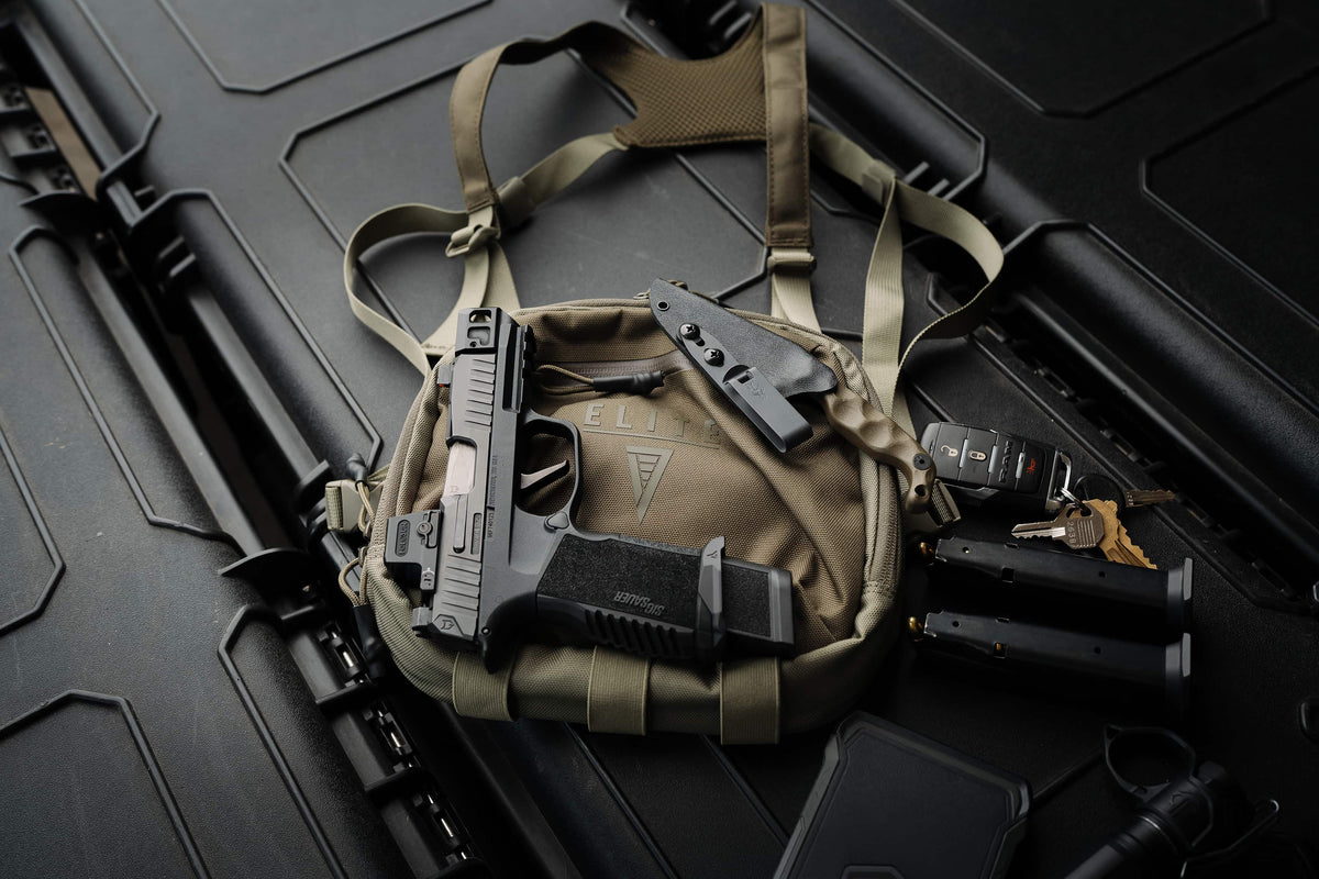 A tan tactical chest rig bag laid flat on a black textured surface, holding a black handgun and other small gear accessories.
