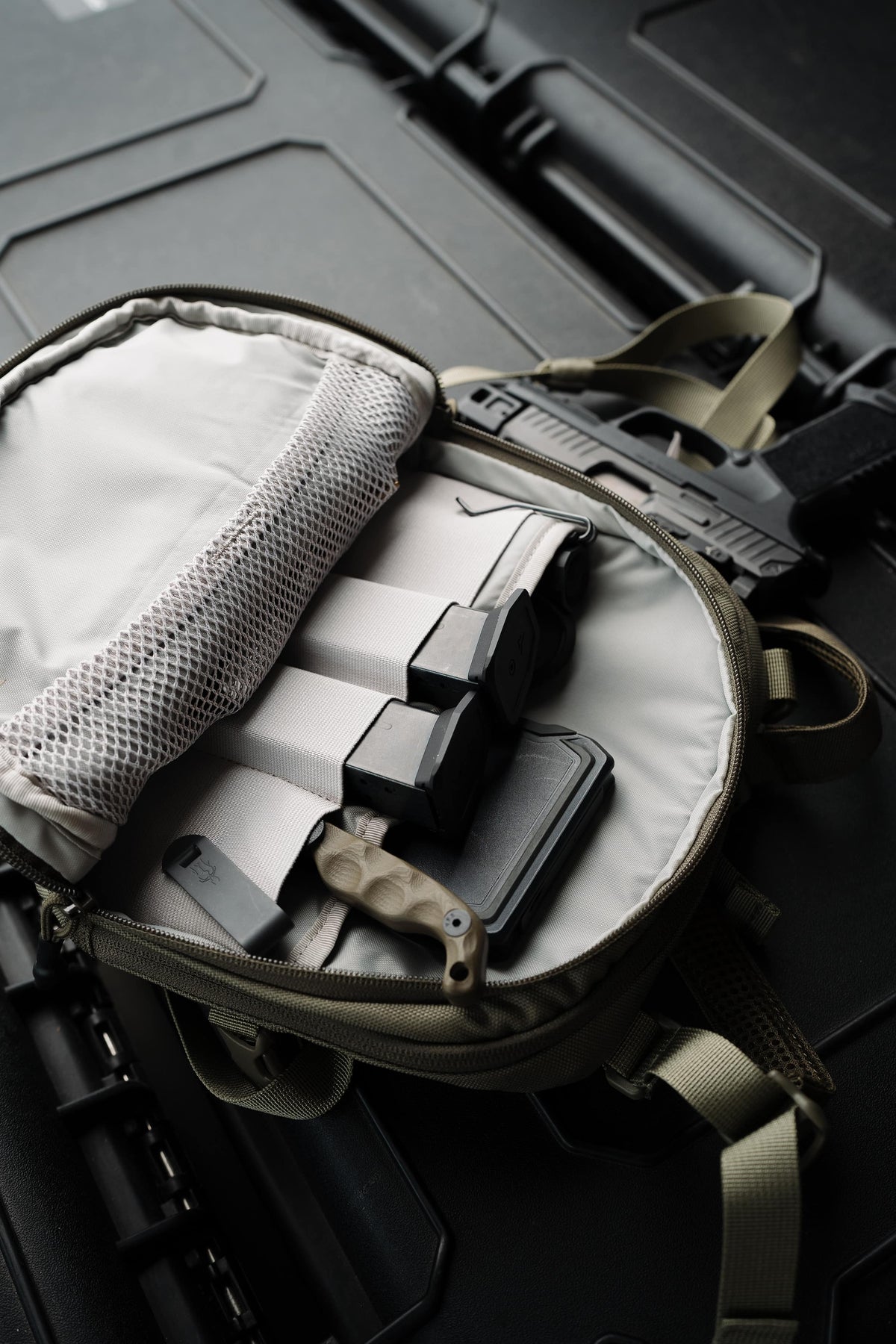 An open tactical bag with a light gray interior organizer, holding black magazines and a knife, set against a dark tactical case background.