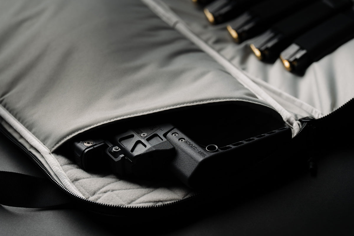 Close-up of a black handgun stored inside an open gray padded zippered case, with additional black cylindrical accessories visible along the upper edge.
