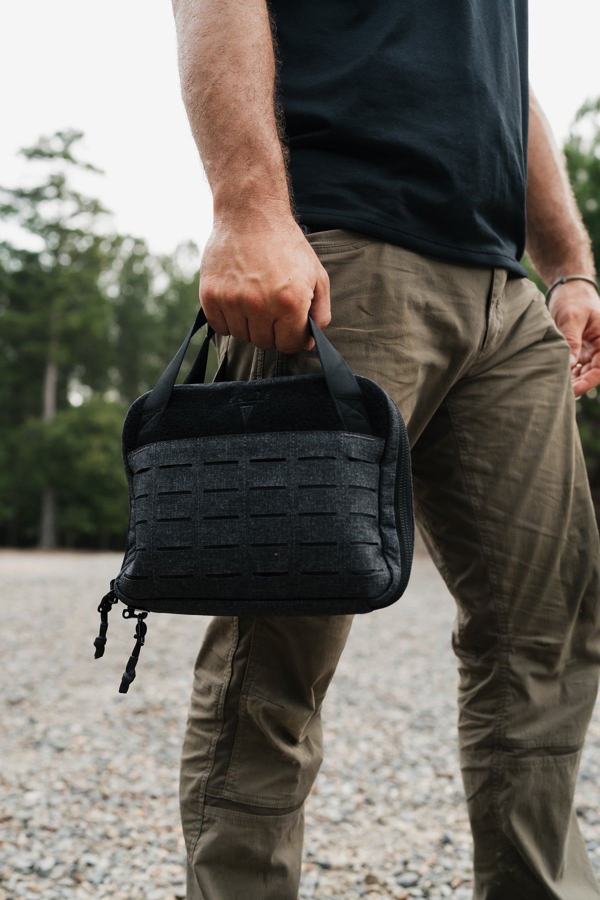 A man outdoors holding a black tactical gear organizer pouch with MOLLE webbing and zipper closure.