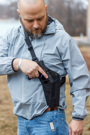 Man in a light gray jacket holding a black gun holster outdoors.