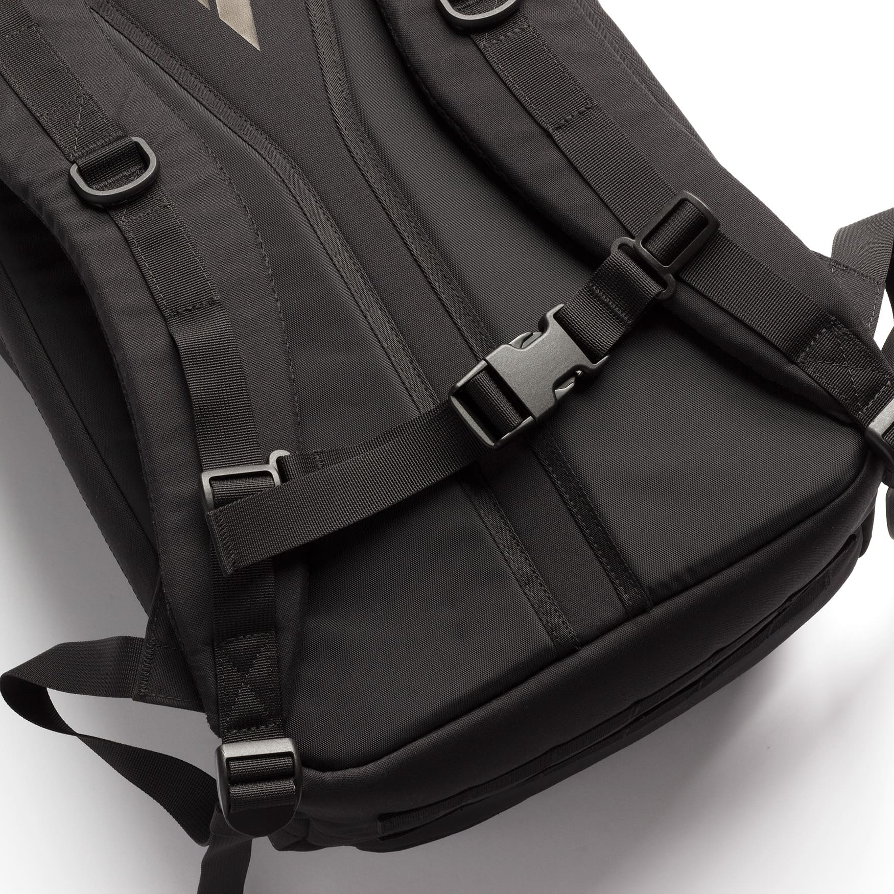 Close-up of a black backpack showing the padded shoulder straps, buckled compression straps, and fabric construction on a white background.