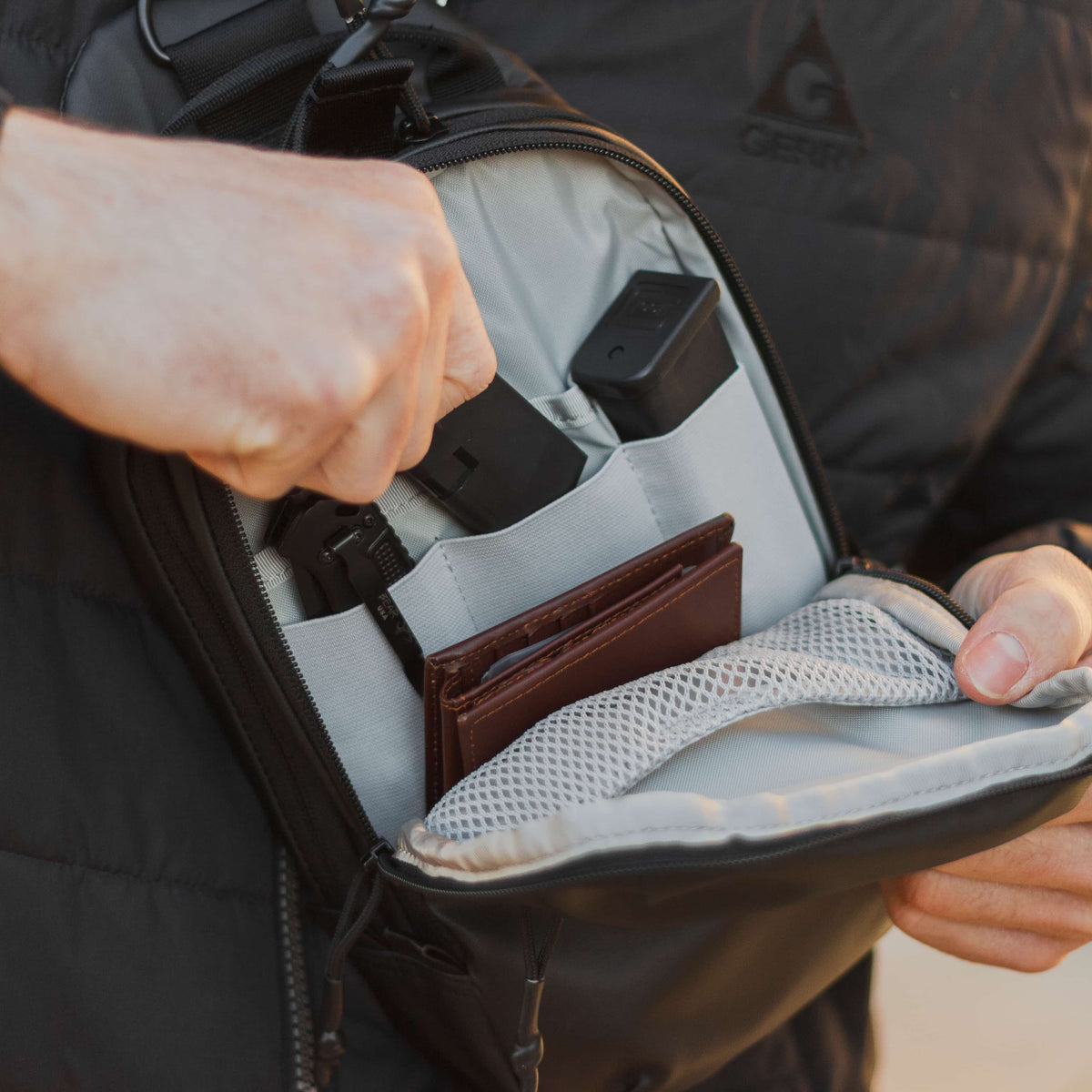 Person opening a backpack to reveal a wallet inside, wearing a black jacket.