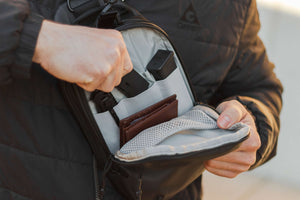 Person opening a backpack to reveal a wallet inside, wearing a black jacket.