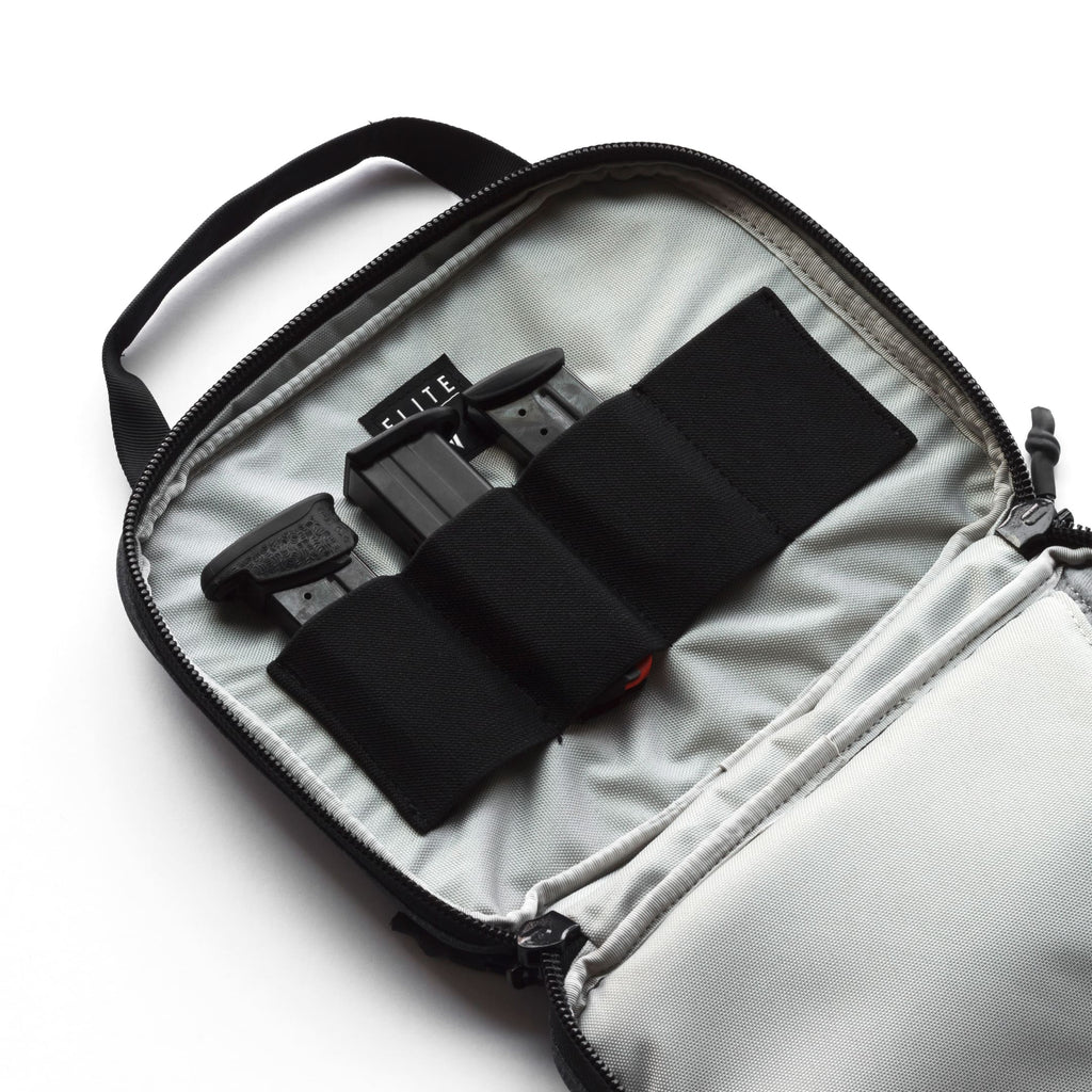 An open light gray camera gear bag with black zippers and black elastic loops holding two black camera accessories. The brand name 'ELITE' is visible on one of the inserts.