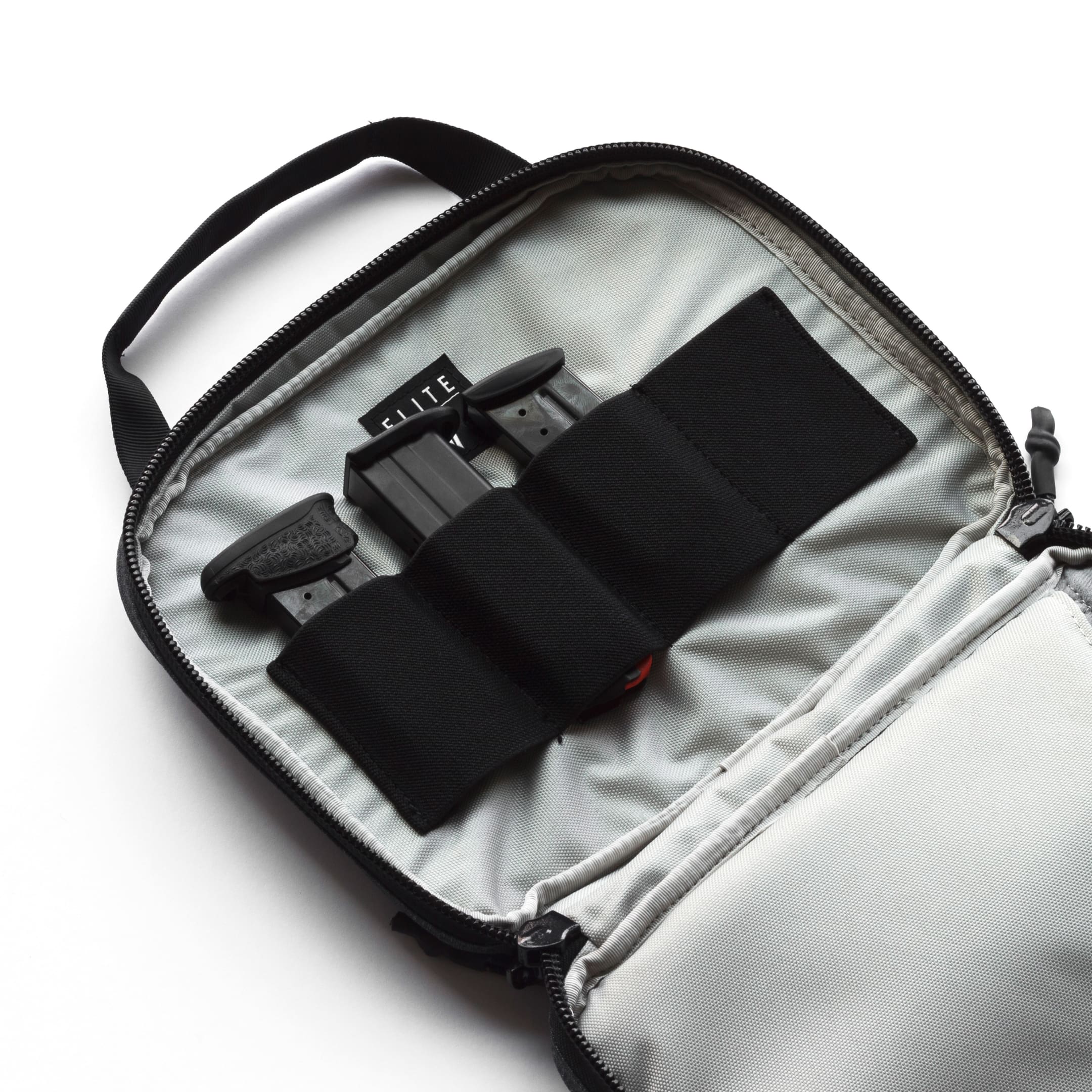An open light gray camera gear bag with black zippers and black elastic loops holding two black camera accessories. The brand name 'ELITE' is visible on one of the inserts.