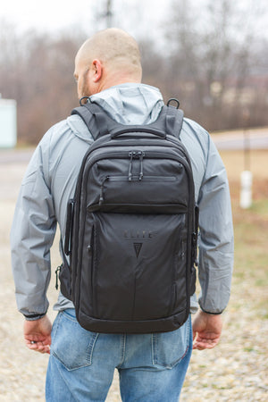 Man wearing a black backpack outdoors on a cloudy day