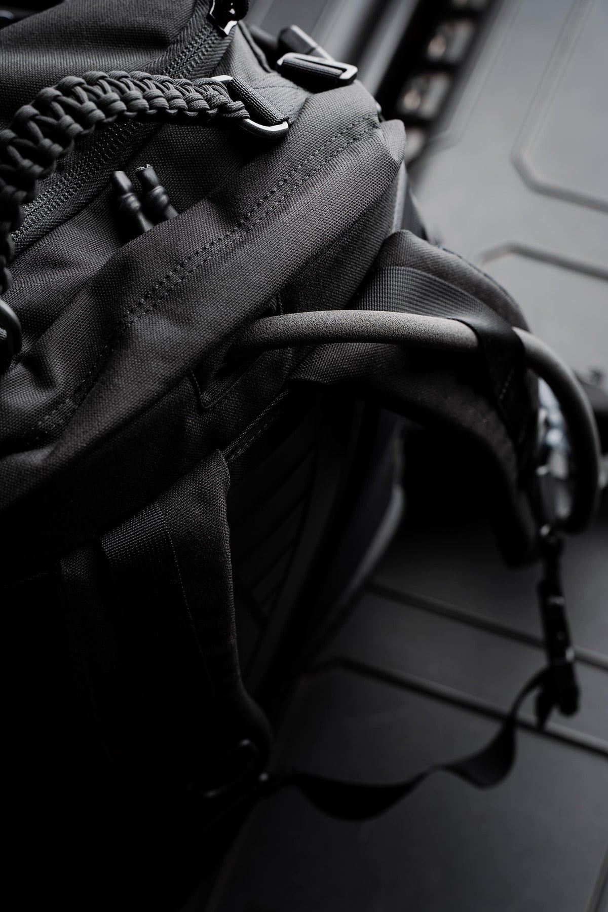 Close-up of the paracord-wrapped grab handle, zipper pulls, and side strap on the black Mission Backpack 40L