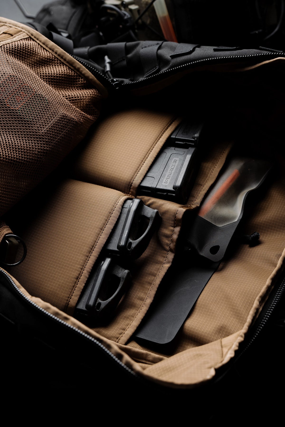Top-down view of the Mission Backpack 40L interior with pistol magazines, a rifle magazine, and a fixed-blade knife in its pouches