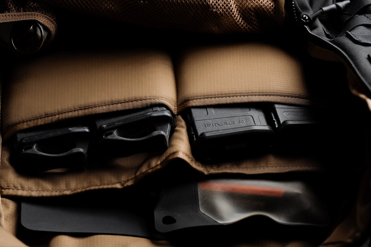 Close-up of the Mission Backpack 40L magazine pouches holding pistol mags and PMAG rifle magazines above a sheathed knife