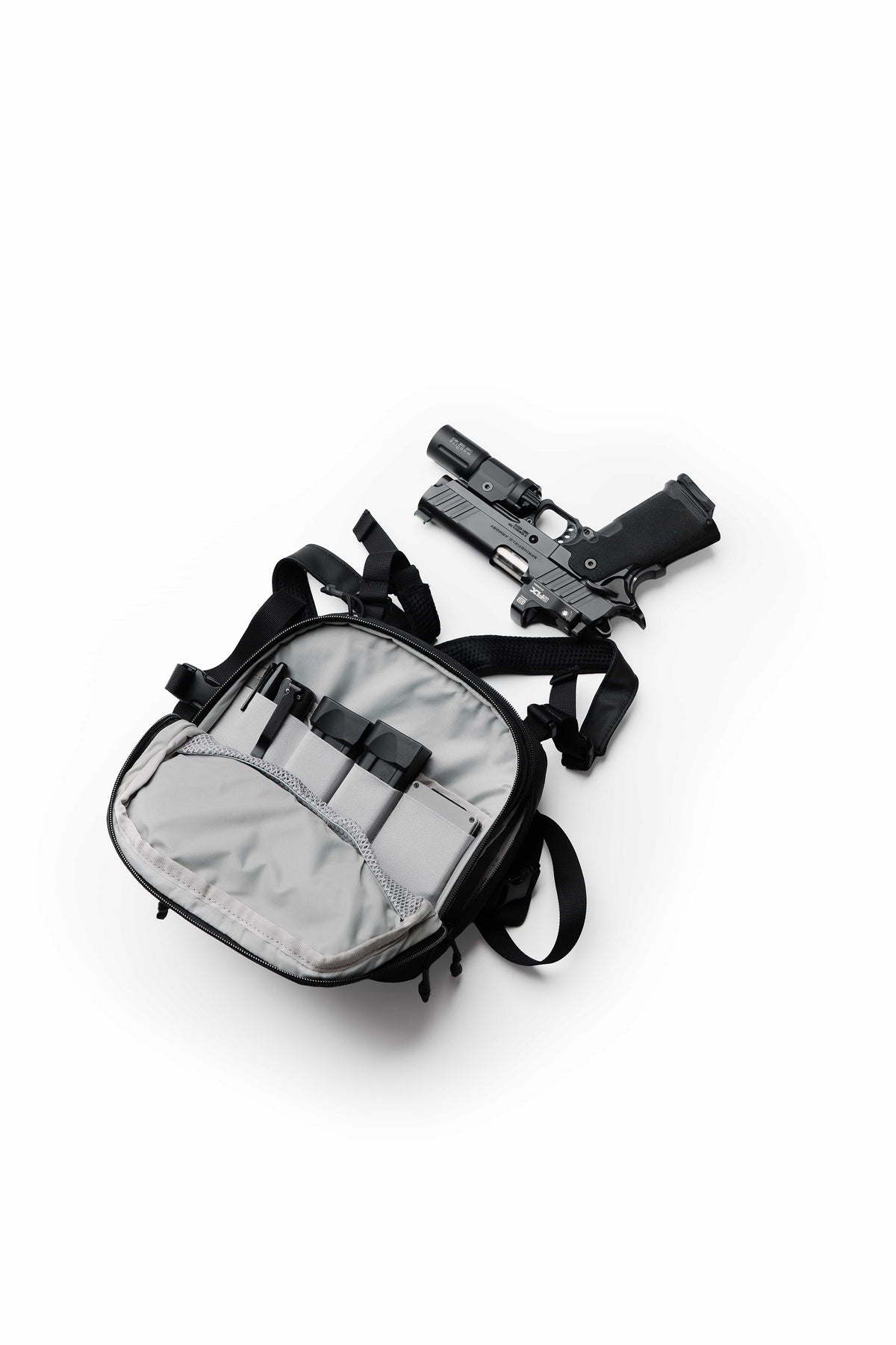 Open front compartment of the black TrailGuard Concealed Carry Chest Holster with elastic loops, beside a handgun with weapon light
