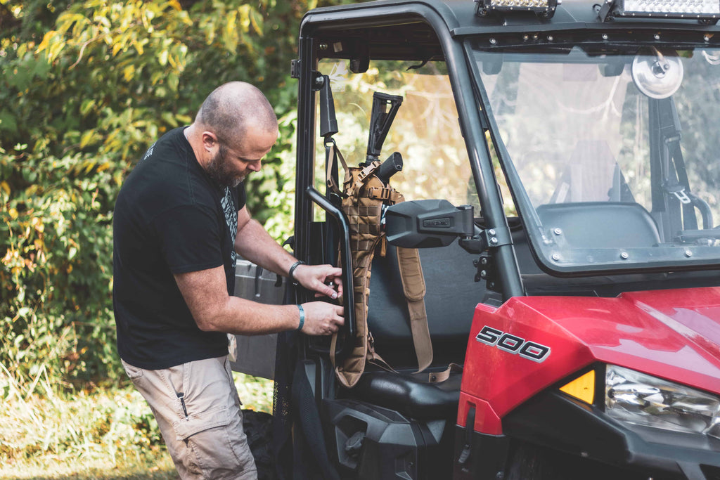 Person adjusting equipment inside a red Polaris vehicle with trees in the background