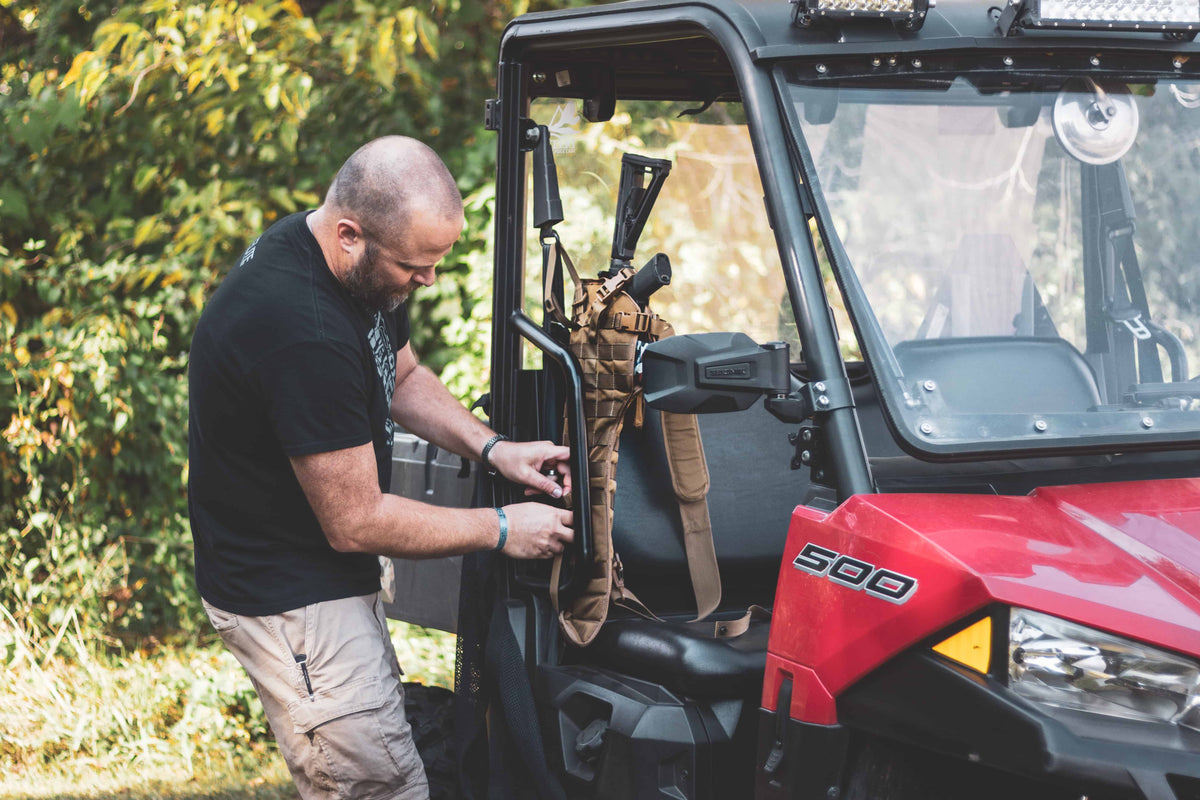 Person adjusting equipment inside a red Polaris vehicle with trees in the background
