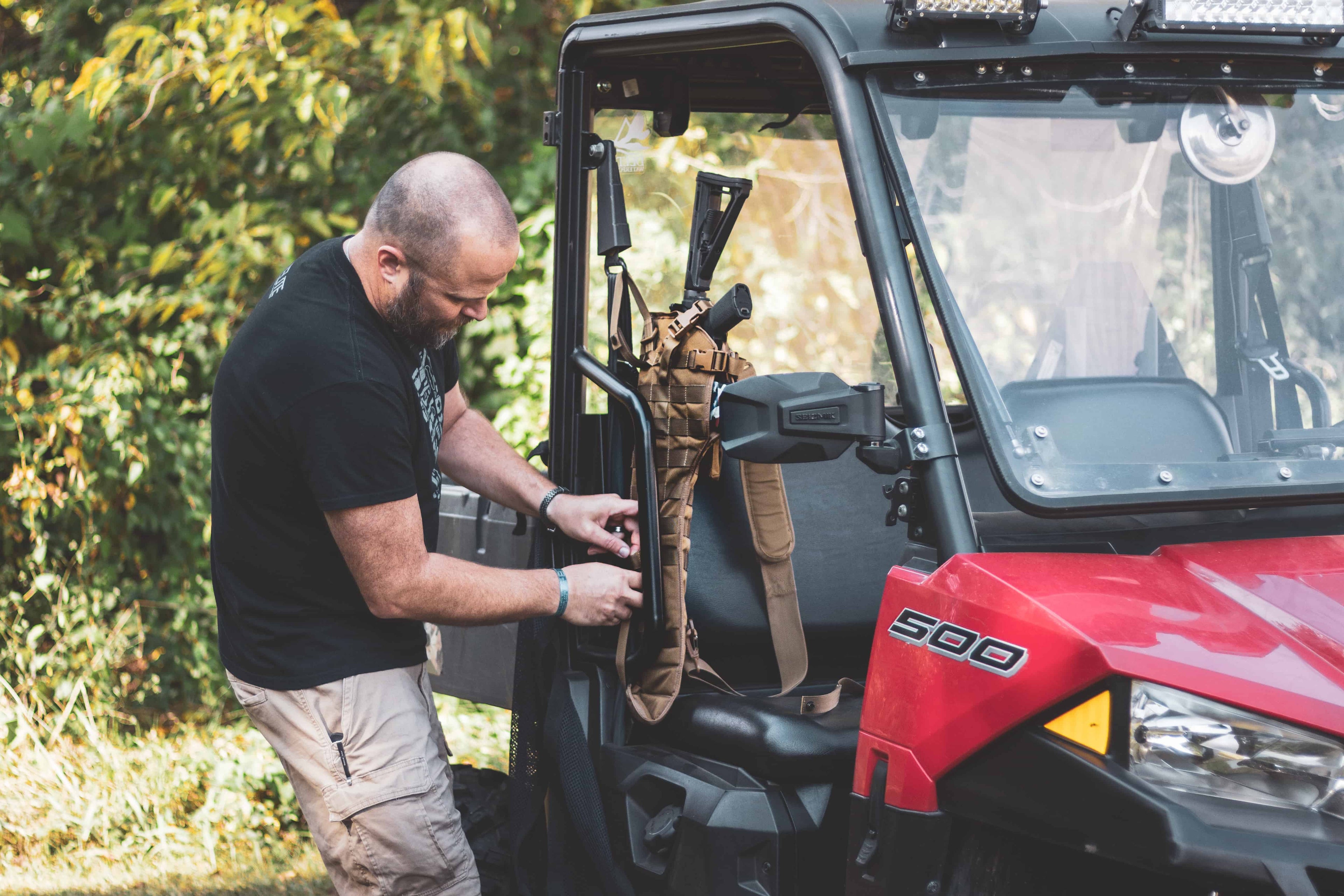 Person adjusting equipment inside a red Polaris vehicle with trees in the background