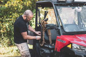 Person adjusting equipment inside a red Polaris vehicle with trees in the background