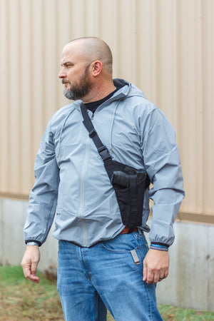 Man wearing a light blue jacket with a black backpack against a beige wall.