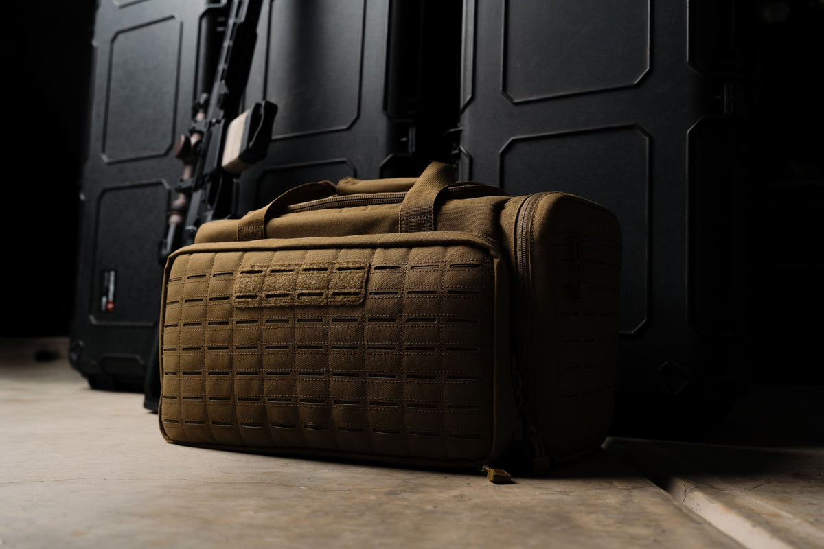 Low-angle view of the Coyote Tan LOADOUT Range Bag with laser-cut MOLLE front panel against black hard rifle cases