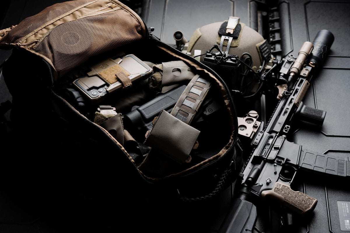 Black Mission 40L backpack unzipped and packed with gear, beside a helmet and a rifle on black hard cases